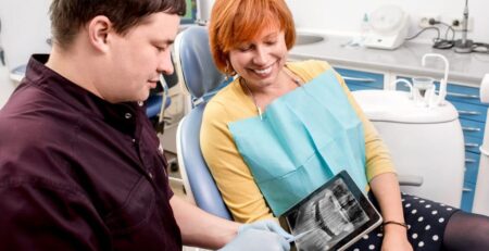 Female watching a tab with x-ray of teeth, and a doctor handling the tab and explaining the issues