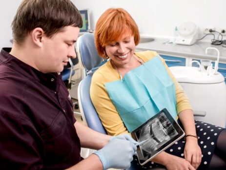 Female watching a tab with x-ray of teeth, and a doctor handling the tab and explaining the issues